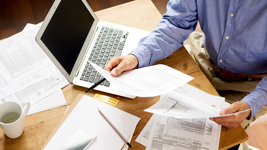 Closeup of unrecognizable senior man filling in application papers at home sitting at table with laptop